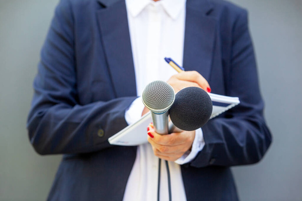 Женщина-журналистка на пресс-конференции или медиамероприятии, пишет заметки, держит микрофон - Фото, изображение