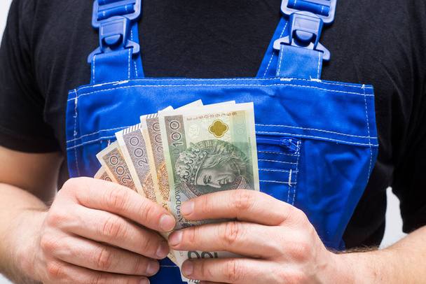 Un lavoratore che prende soldi polacchi dalle tasche dei suoi pantaloni da lavoro, il concetto di stipendi e costi dei professori - Foto, immagini