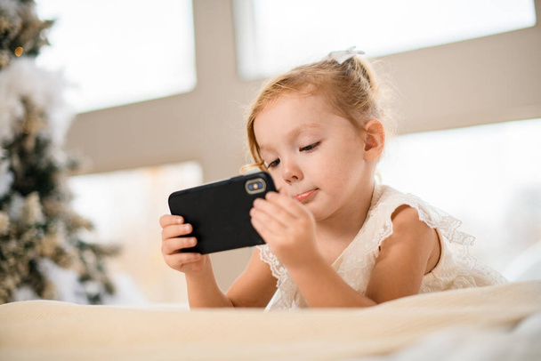 close-up view of little girl who holds phone and looks at screen - Фото, изображение