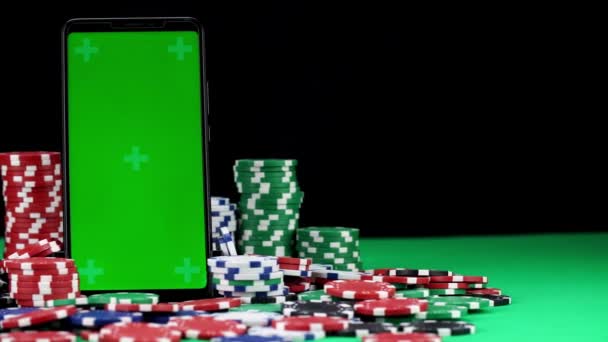 Крупный план мобильного телефона с хрома-ключом в вертикальной ориентации среди кучи фишек для покера - Кадры, видео