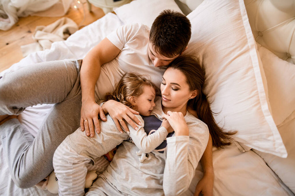 view of young married couple with small child in pajamas lying on the bed - Photo, image