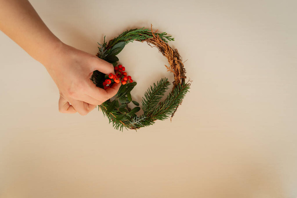 モミやトウヒの枝やサンザシのトップビューでクリスマスリースを準備する若い女性写真 - 写真・画像