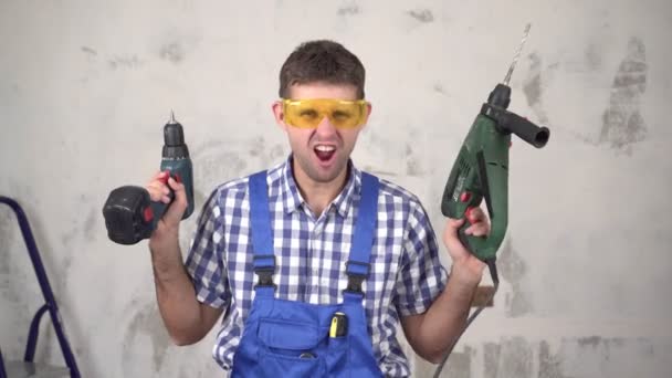 Смешной веселый эмоциональный работник мужского пола или строитель с электроинструментами на фоне ремонта в доме - Кадры, видео