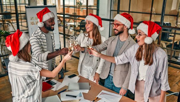Veselé Vánoce a šťastný nový rok! Multiraciální mladí tvůrčí lidé slaví dovolenou v moderní kanceláři. Skupina mladých podnikatelů pije ve spolupráci šampaňské. - Fotografie, Obrázek