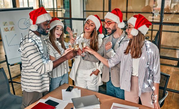 Mutlu Noeller ve mutlu yıllar! Çok ırklı genç yaratıcı insanlar modern ofiste bayramı kutluyorlar. Bir grup genç iş adamı birlikte çalışarak şampanya içiyor.. - Fotoğraf, Görsel