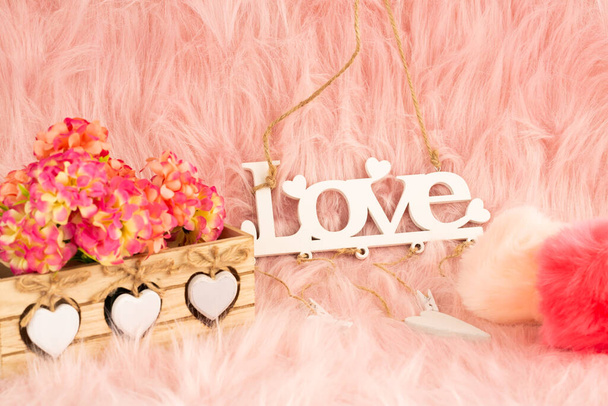 Valkoinen puinen sana rakkaus, laatikko, kukat ja pörröiset pallot vaaleanpunaisella turkistaustalla. - Valokuva, kuva