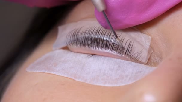 Face of a young girl before a modern eyelash lamination procedure in a professional beauty salon. The master applies special glue before the eyelash curling procedure in pink rubber gloves close up - Footage, Video