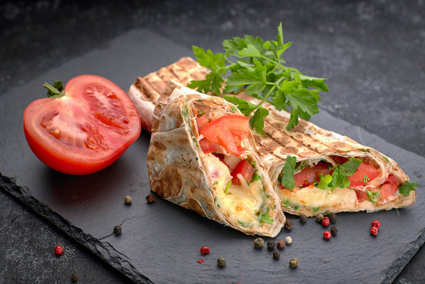Shawarma cutaway, with sauce, tomatoes, cheese, herbs and garlic, on black slate, on a black background - 写真・画像