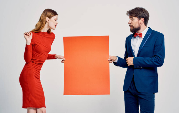 Een elegante man in een pak en een vrouw in een rode jurk met een klaproos in hun handen een poster voor een advertentie - Foto, afbeelding
