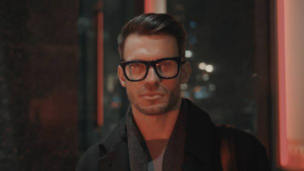 Businessman in coat and eyeglasses gimbal shot with red night lights - Foto, afbeelding