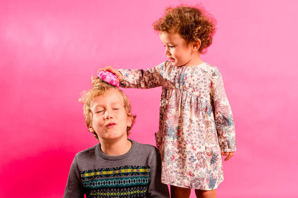 Μικρή αδελφή βοηθά το μεγαλύτερο αδελφό της χτένισμα μαλλιά του, αστεία εικόνα της οικογένειας. - Φωτογραφία, εικόνα