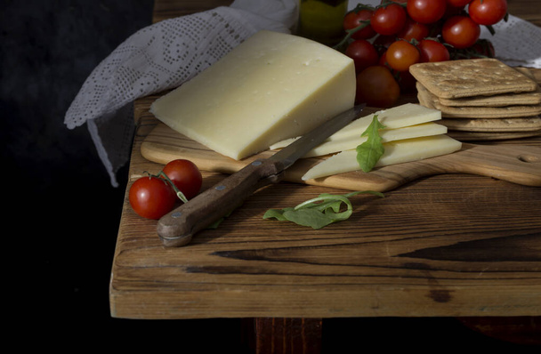 Queso duro fresco, cuchillo, tomates cherry y galletas saladas en una mesa de madera - Foto, Imagen
