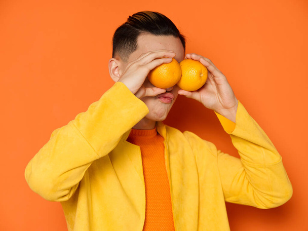 A man in a yellow jacket on an orange background with fruits in front of his eyes - Zdjęcie, obraz