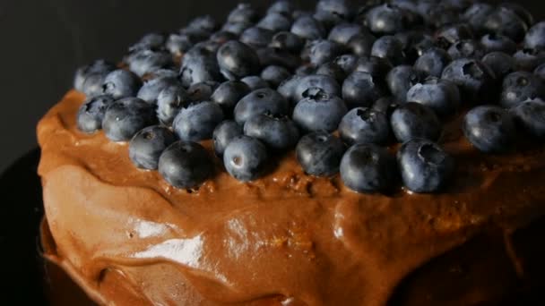 Close-up uitzicht op brownie chocolade taart met cacao glazuur en bosbessen op stijlvolle zwarte achtergrond in low-key - Video