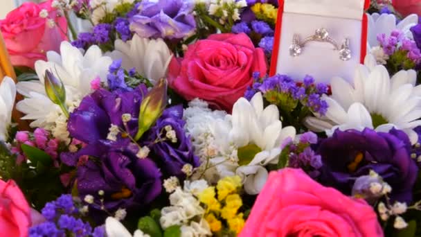 Bovenaanzicht van cadeau aanwezig rode doos met een set van verlovingsring en oorbellen op de achtergrond van een veelkleurig mooi boeket bloemen. Huwelijksaanzoek, een nieuw gelukkig leven. - Video