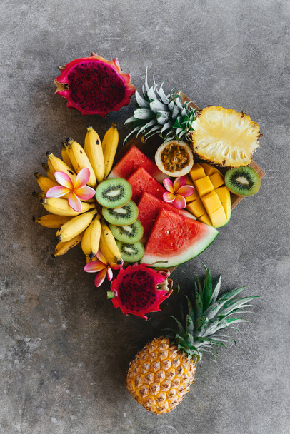 Tropical fruits assortment on a wooden plate. Stone background. - Valokuva, kuva