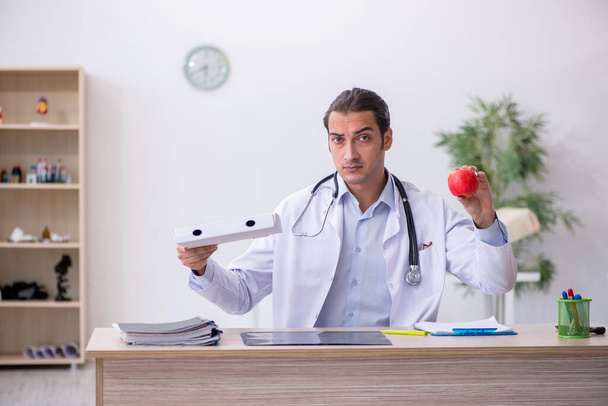 Young male doctor dietician holding apple and pizza box - Photo, Image