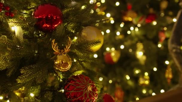 Close-up van verschillende rode plastic kerstspeelgoed opknoping op een kunstmatige kerstboom. Voorraadvideo. Kleurrijke decoraties en bloemenslingers. Gekleurde kerstversieringen. Bauble. Gelukkig Nieuwjaar. Vakantie - Video