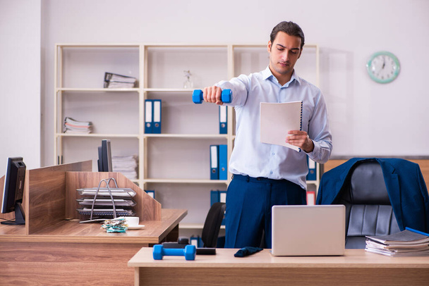 Young male employee doing physical exercises at workplace - Photo, Image