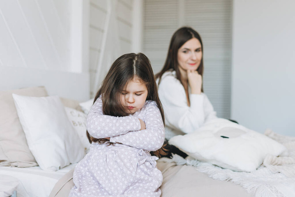 Cute hurt long hair little girl with her mother at bright bed room, negative emotion - Foto, Imagem