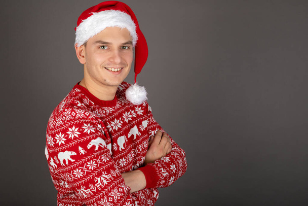 Handsome young man wearing Santa hat and red Christmas style pullover on grey background - 写真・画像