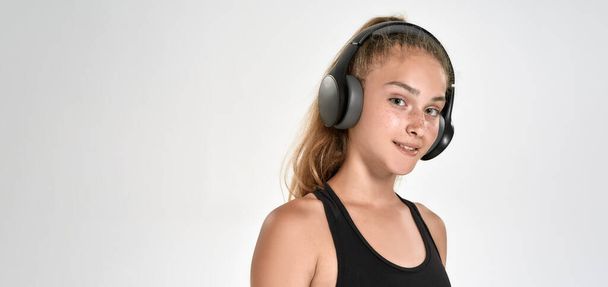 Portrait of cute sportive girl child wearing headphones, listening to music, looking at camera while posing isolated over white background - Zdjęcie, obraz