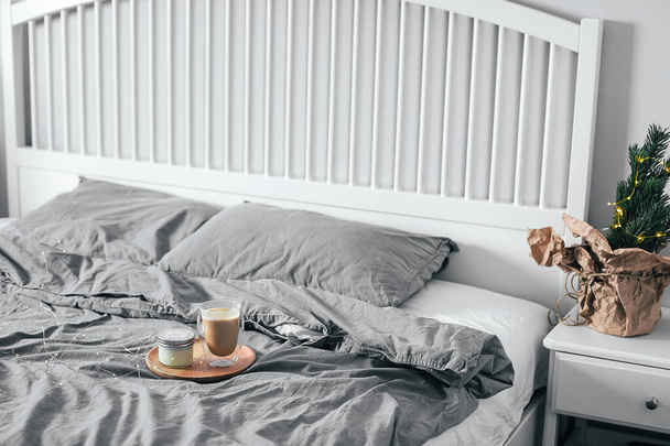 Bandeja de madera con vaso de café y vela en la cama en el dormitorio. Interior escandinavo ligero. Rutina matinal. - Foto, Imagen