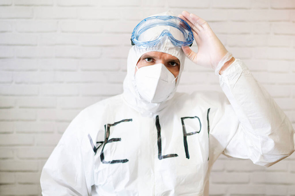 Male nurse wearing protective suit and work clothes while standing and writing help on chest - Photo, Image