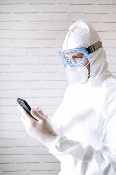 Чоловіча медсестра носить захисний костюм і робочий одяг за допомогою смартфона
 - Фото, зображення