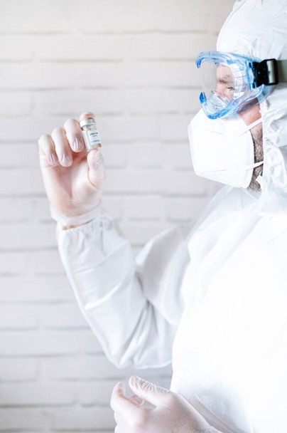 Pielęgniarka w kombinezonie ochronnym patrzy na fiolkę szczepionki przeciwko kovid19 - Zdjęcie, obraz