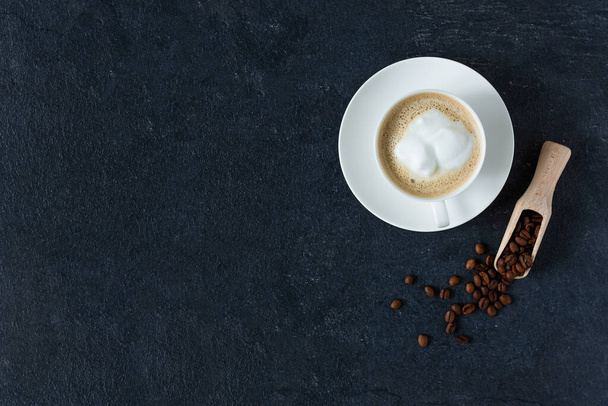 Kahvikuppi maitoa ja paahdettuja kahvipapuja mustalla taustalla ylhäältä näkymä. Kuppi tasainen valkoinen kahvi.  - Valokuva, kuva