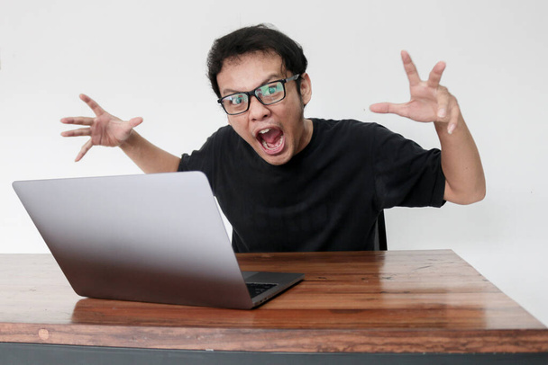 Young Asian man is Angry and hate with laptop. Indonesia Man wear black shirt Isolated grey background. - 写真・画像
