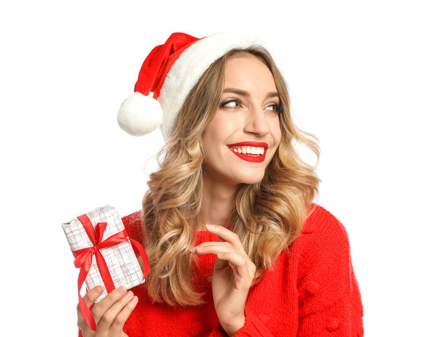 Happy young woman wearing Santa hat with Christmas gift on white background - Fotoğraf, Görsel