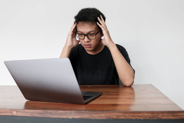 Young Asian man feeling stress and confuse with work in laptop. Indonesia Man wear black shirt Isolated grey background. - Foto, Imagen