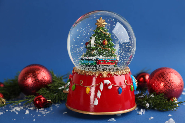Beautiful snow globe, Christmas balls and coniferous twigs on blue background - Foto, imagen