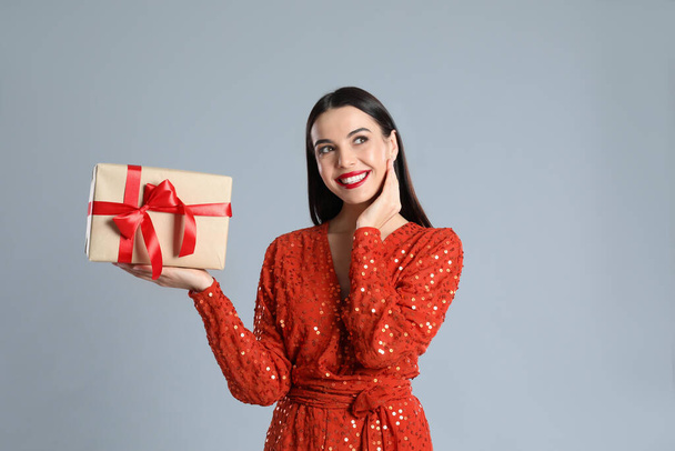 Woman in red dress holding Christmas gift on grey background - Photo, Image