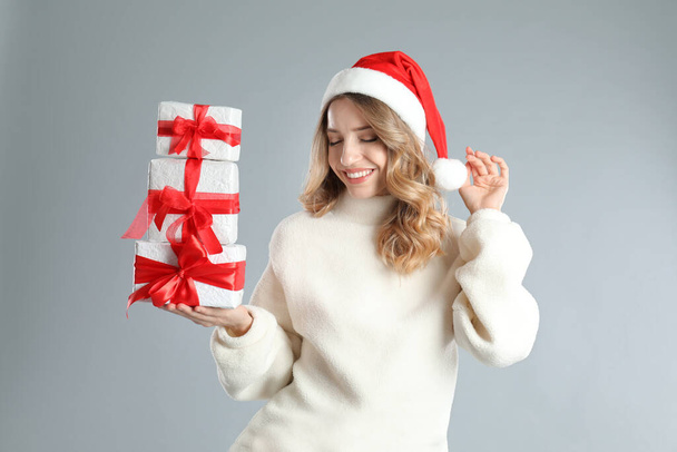Beautiful young woman in Santa hat with Christmas presents on light grey background - Fotoğraf, Görsel