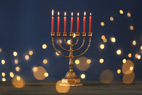 Golden menorah with burning candles on table against blue background and blurred festive lights - Fotoğraf, Görsel