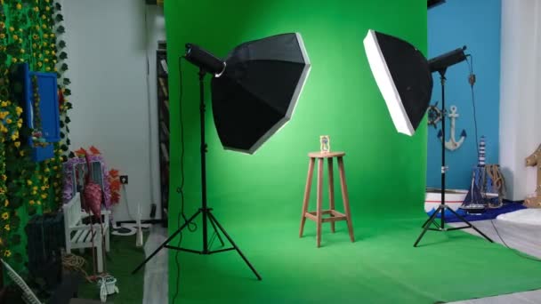Altı köşeli stüdyo ışıkları olan fotoğraf ya da video stüdyosu. Yeşil perdede kum saati ve sabitlenmiş sandalye - Video, Çekim