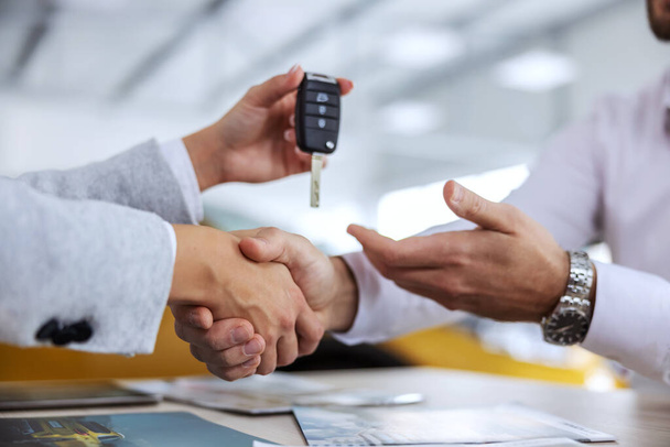 Closeup of car seller and buyer shaking hands. Car seller handing a car keys to a buyer. Car salon interior. - Fotoğraf, Görsel