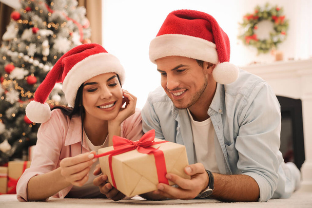 Happy couple in Santa hats with Christmas gift at home - Fotó, kép