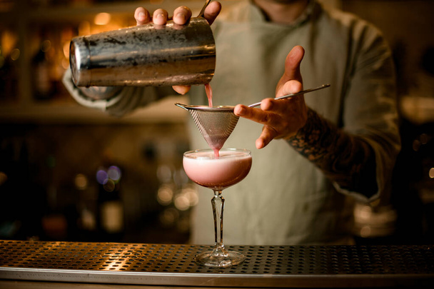 bartender holds sieve over wine glass and carefully pours cocktail from shaker. - 写真・画像