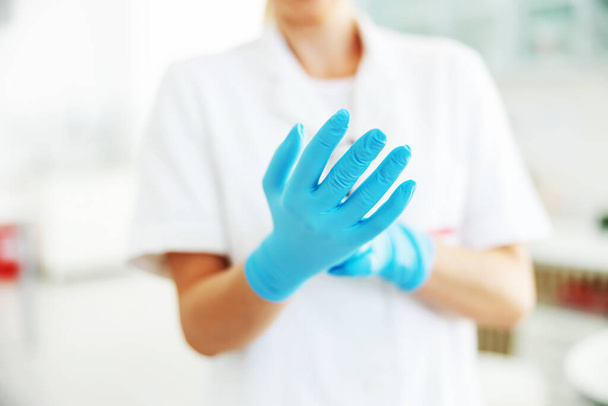 Zbliżenie asystenta laboratoryjnego zakładającego sterylne gumowe rękawiczki. - Zdjęcie, obraz