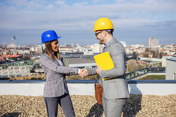 Young heterosexual business partners standing on rooftop and shaking hands. They making agreement. - Fotoğraf, Görsel