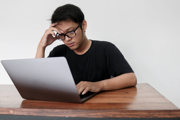 Young Asian man is boring and lazy in the front the laptop. Indonesia Man wear black shirt Isolated grey background. - Fotoğraf, Görsel