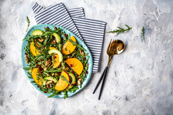 Gourmet salad with persimmon, avocado, pumpkin seeds, walnuts, pomegranate and arugula on a light background, Flat lay. Banner. Top view. - Photo, Image