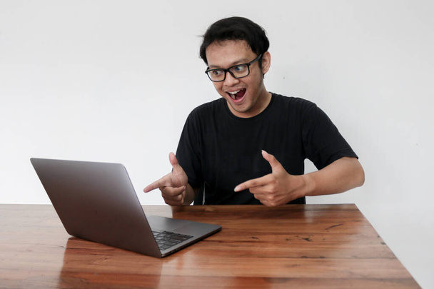 Young Asian man feeling happy and smile when work laptop on table. Indonesian man wearing blue shirt. - Fotó, kép