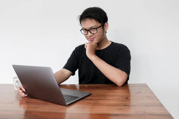 Young asian man is smile and enjoy when working at home with laptop and a cup of coffee. A man sitting on bed and working. Work from home concept. - Photo, image