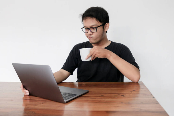 Young asian man is smile and enjoy when working at home with laptop and a cup of coffee. A man sitting on bed and working. Work from home concept. - Foto, imagen