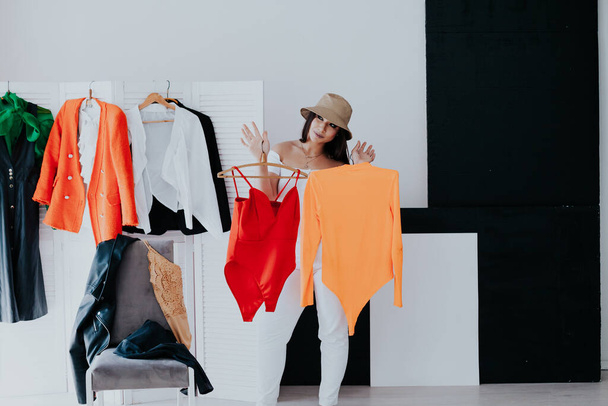 Portrait of happy young smiley brunette woman choosing outfit from wardrobe closet with stylish clothes - Photo, Image